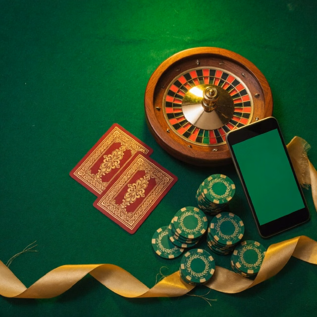 Roulette wheel, cards and green chips on a dark felt table with a phone in front